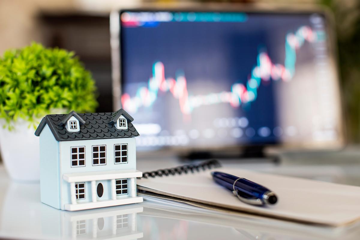 House model, pen and notepad on table with stock market chart